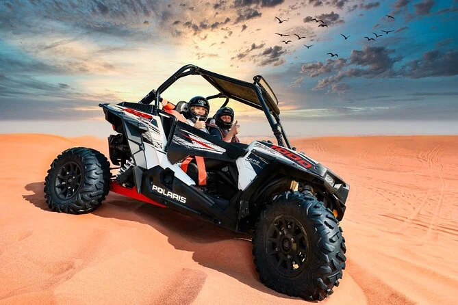 Two helmeted visitors in a Polaris buggy on the sand