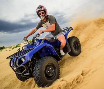 A rider on a blue quad bike descending a sandy dune
